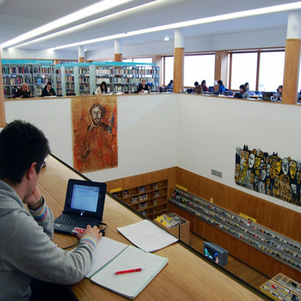 Rapaz sentado a estudar num computador portátil, na Biblioteca Almeida Garrett com mais estudantes