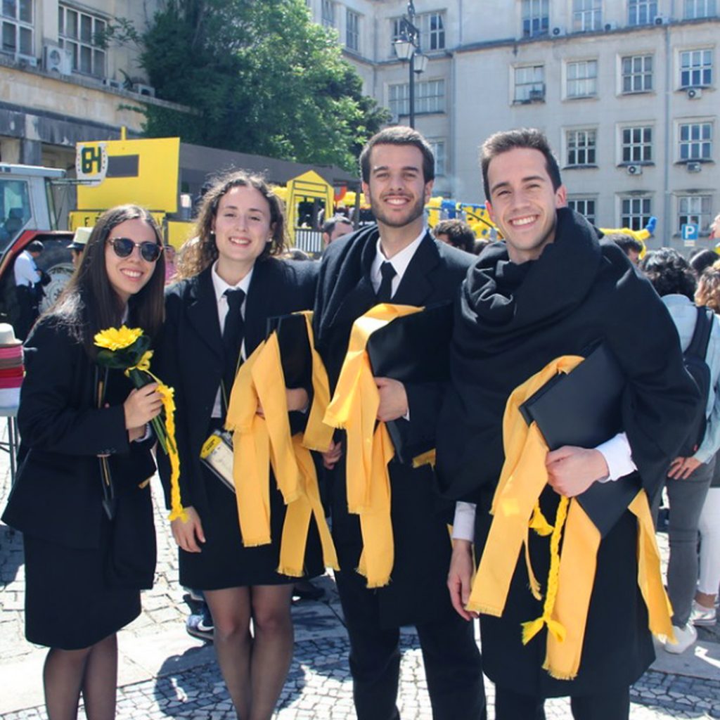 Quatro jovens vestidos de traje académico, com pastas e fitas, na Queima das fitas Coimbra