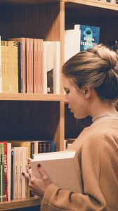 Plano fechado sobre rapariga junto de prateleira de livros, numa biblioteca