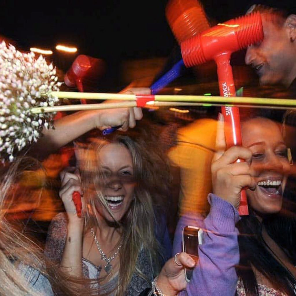 Imagem dinâmica, com duas jovens a festejar as festas de São João do Porto com martelos de plástico